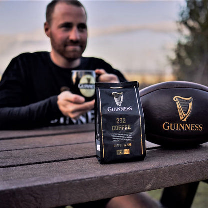 A rugby fan sitting on a picnic table with a limited-edition bag of Guinness Ground Coffee 227g.