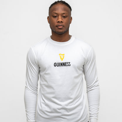 A person faces forward in the Guinness Seb Curi Lovely Day Longsleeve Tee - White from Guinness Webstore US, featuring the brand’s iconic logo and text on the front, against a plain white background.