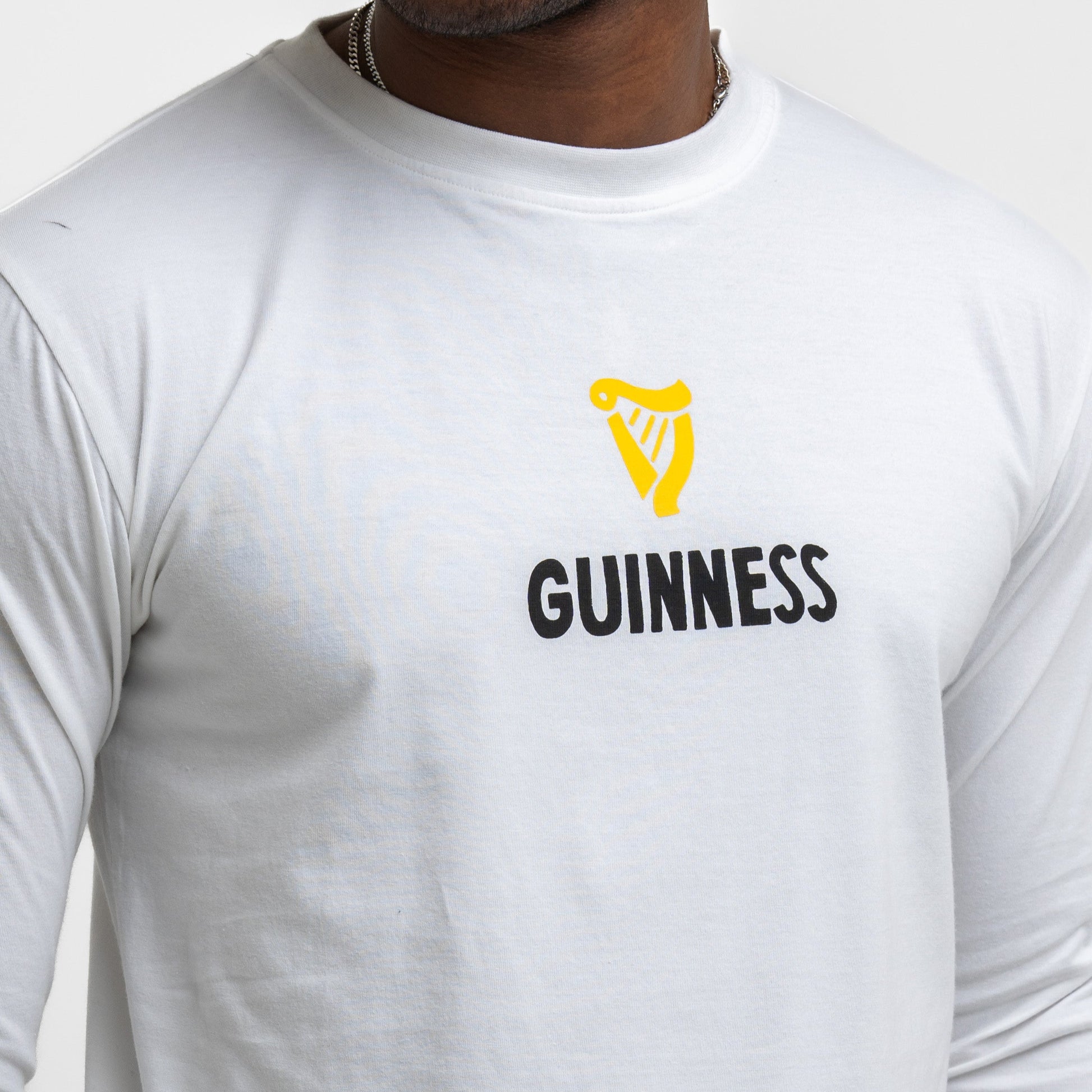 Someone wearing the Guinness Seb Curi Lovely Day Longsleeve Tee in white from Guinness Webstore US, featuring a yellow harp and "GUINNESS"—a stylish wearable art piece.