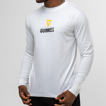 A person wears the Guinness Seb Curi Lovely Day Longsleeve Tee in white from Guinness Webstore US, featuring a yellow harp logo and "GUINNESS" on the front—a unique design from the Sebastian Curi collaboration.