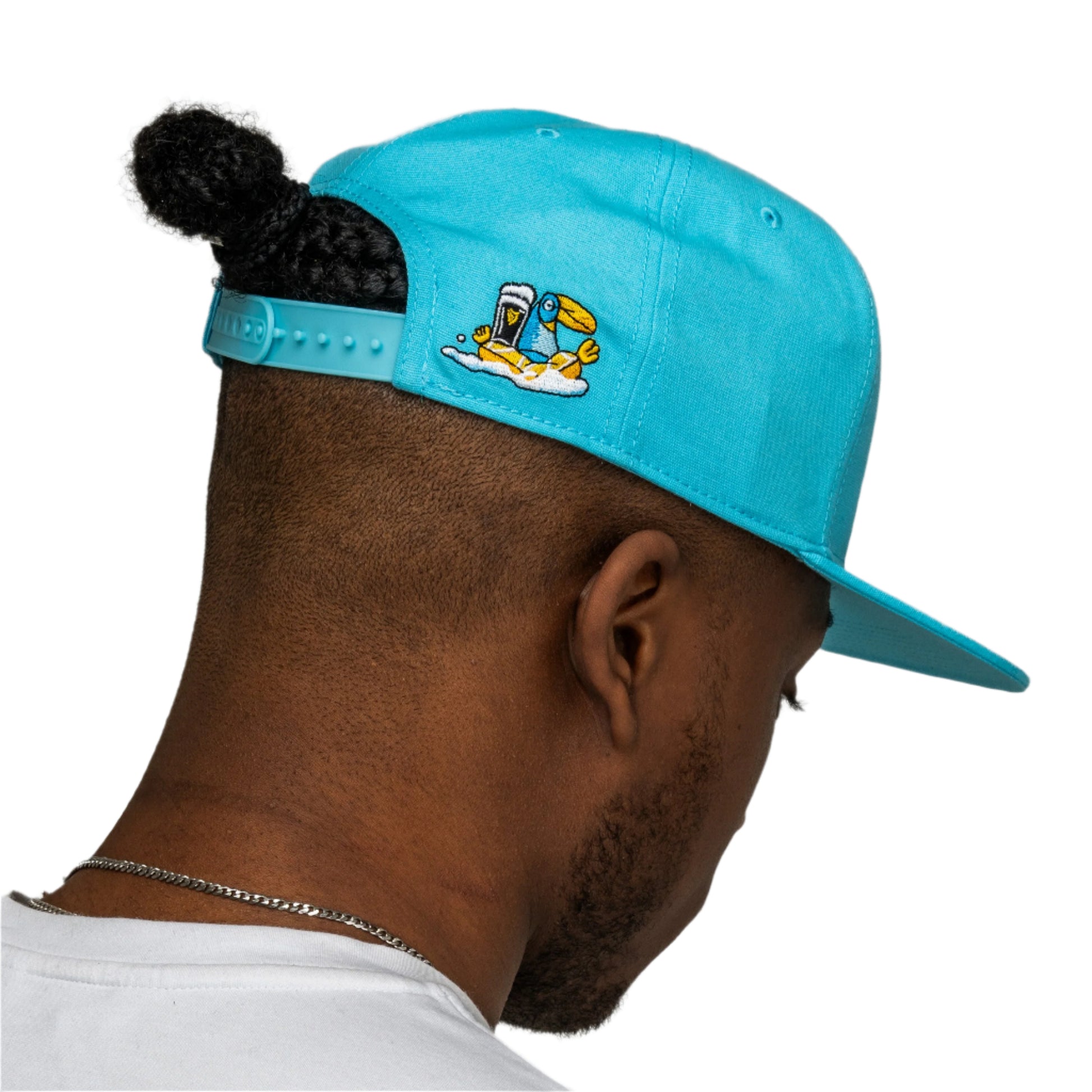 A person with dark hair in a bun, facing away from the camera, wears a bright blue Guinness Seb Curi Lovely Day Flat Brim Cap by Guinness Webstore US featuring a cartoon bird with a spray can.