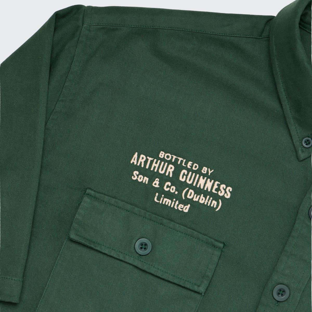 The Guinness Cooperage Work Shirt is a green heavyweight cotton shirt with a chest pocket and cream embroidery: “Bottled by Arthur Guinness Son & Co. (Dublin) Limited.”.