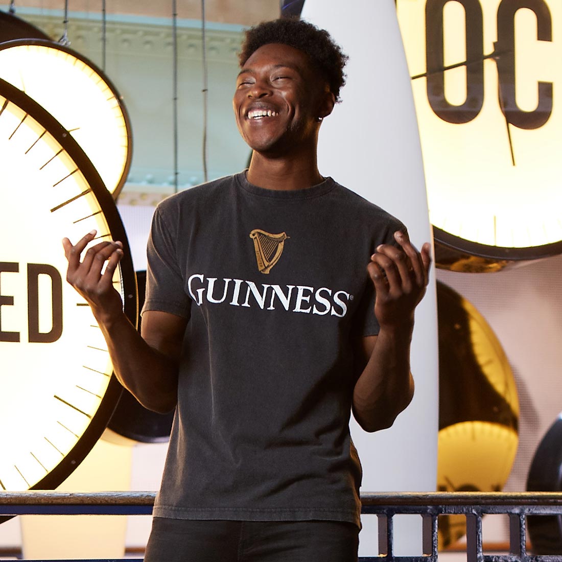 A man in a distressed Guinness® Distressed Trademark Label T-Shirt standing in front of a clock.