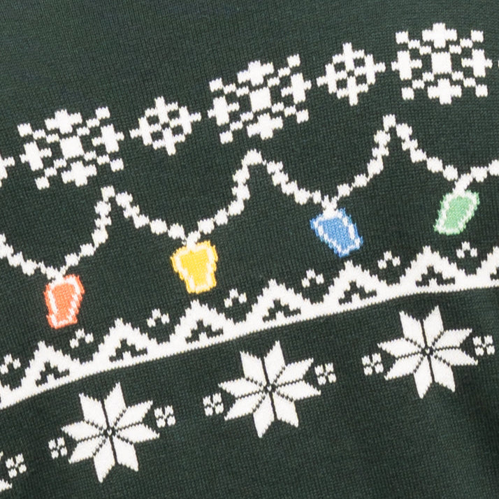 A close-up of the Guinness Holiday Pint Lights Sweater - Green from Guinness Webstore US, featuring dark green fabric, white snowflake patterns, and a row of bright red, yellow, blue, and green Christmas lights.