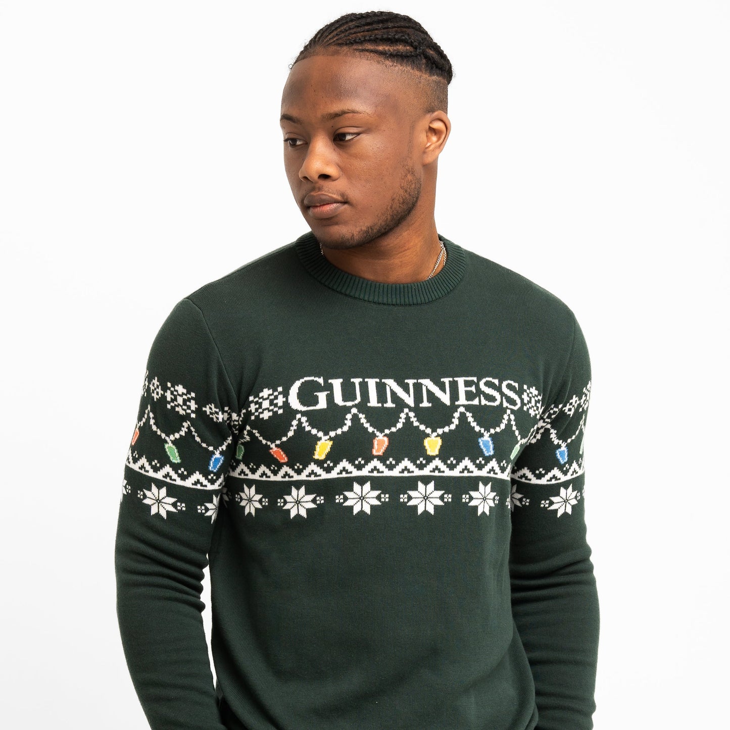 A person wears the Guinness Holiday Pint Lights Sweater - Green by Guinness Webstore US, featuring "GUINNESS," snowflakes, and colorful holiday lights—perfect for anyone wanting a festive look.