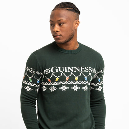A person wears the Guinness Holiday Pint Lights Sweater - Green by Guinness Webstore US, featuring "GUINNESS," snowflakes, and colorful holiday lights—perfect for anyone wanting a festive look.
