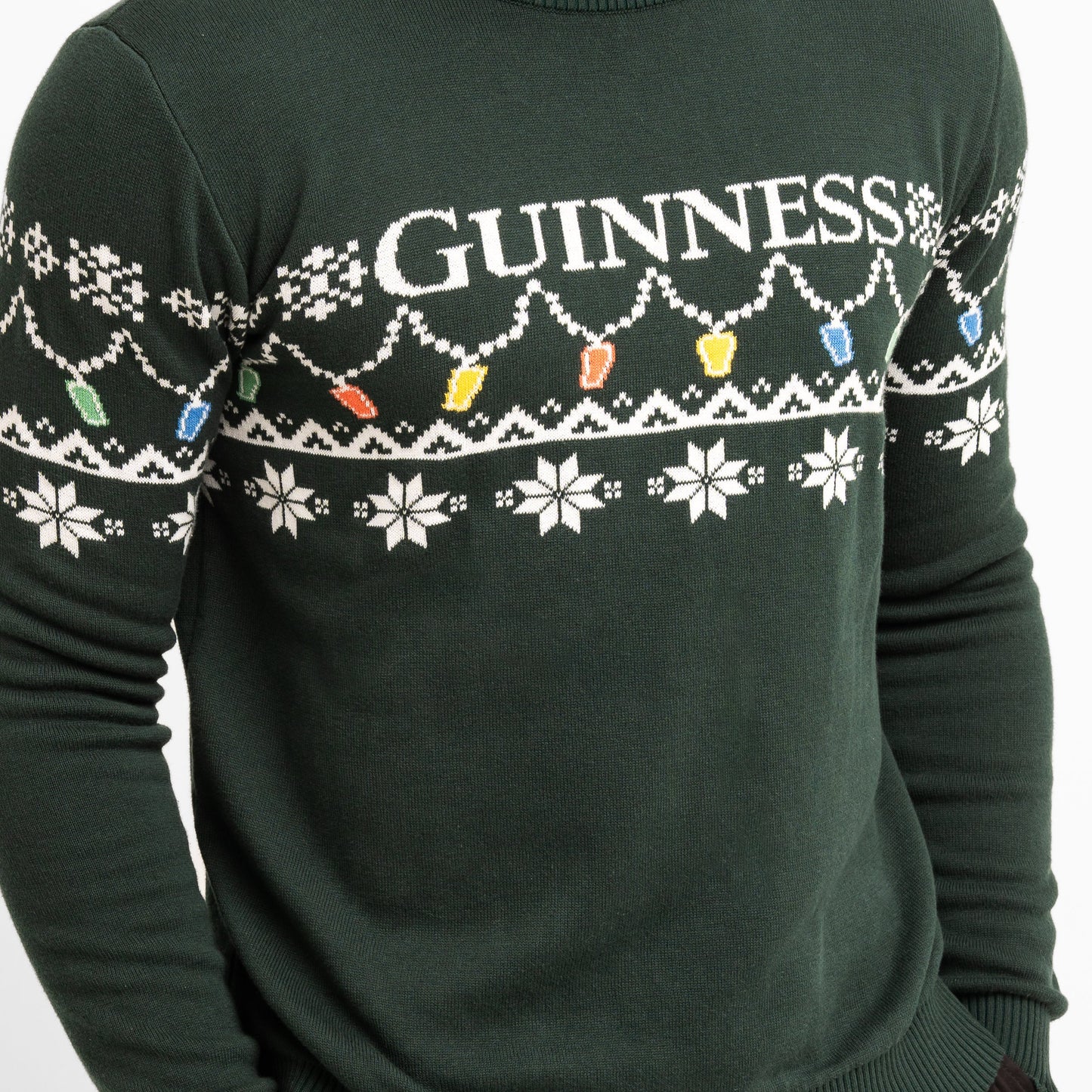 Celebrate the season in the Guinness Holiday Pint Lights Sweater - Green from Guinness Webstore US, featuring festive "GUINNESS" text, white snowflakes, and colorful holiday lights.
