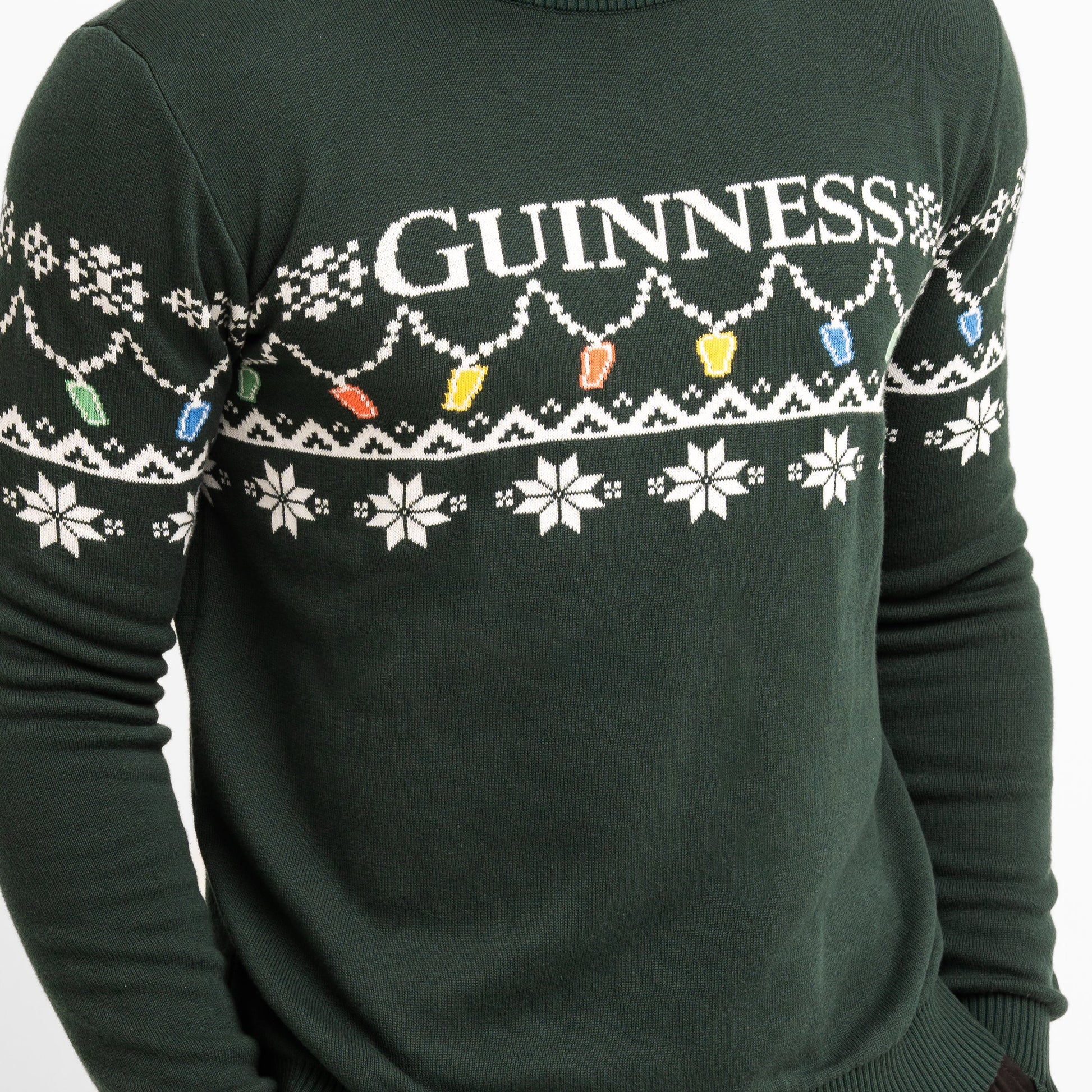 Celebrate the season in the Guinness Holiday Pint Lights Sweater - Green from Guinness Webstore US, featuring festive "GUINNESS" text, white snowflakes, and colorful holiday lights.