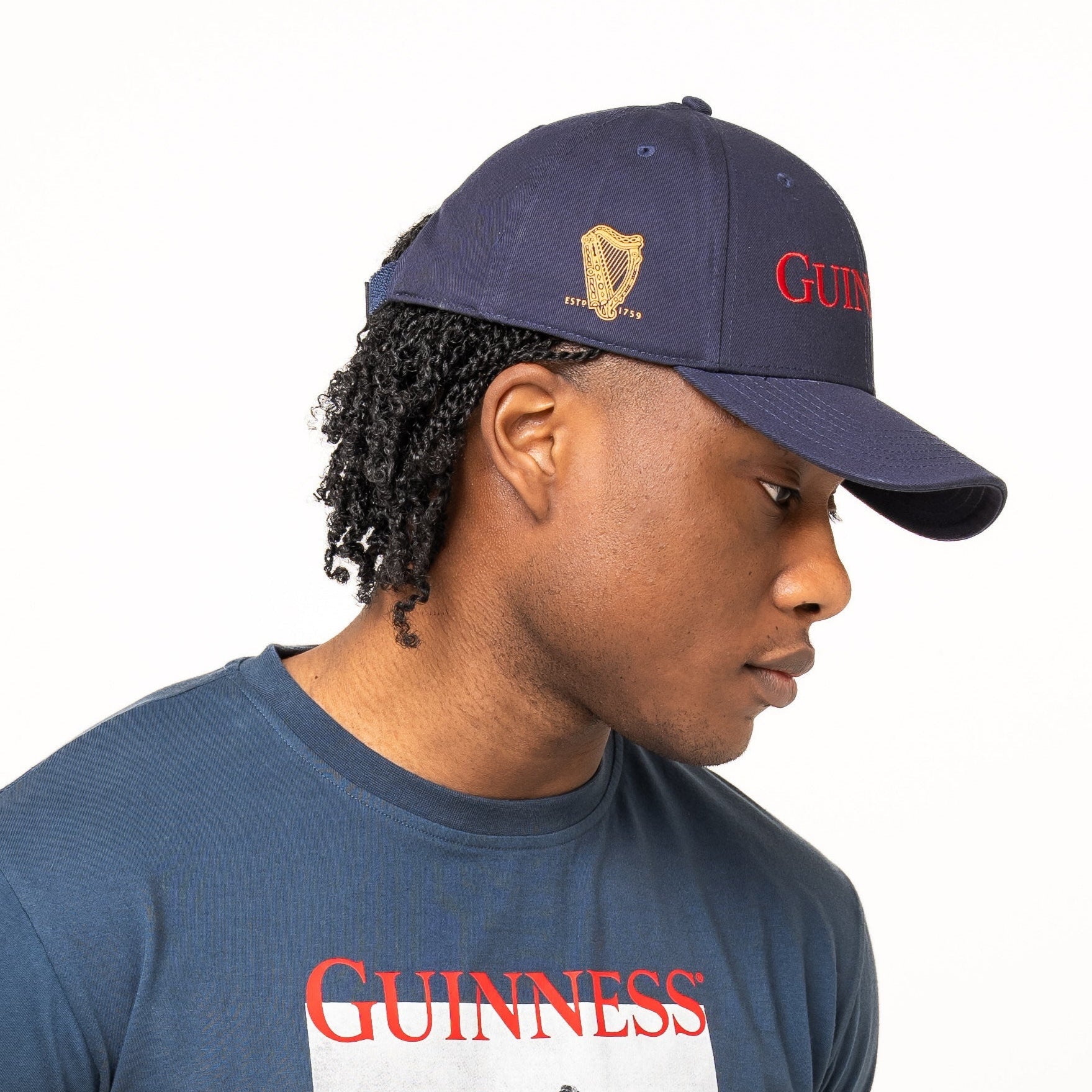 A person wearing a navy Guinness T-shirt with a vintage print and the timeless Guinness Transport Collection Baseball Cap by Guinness Webstore US, standing against a plain white background.
