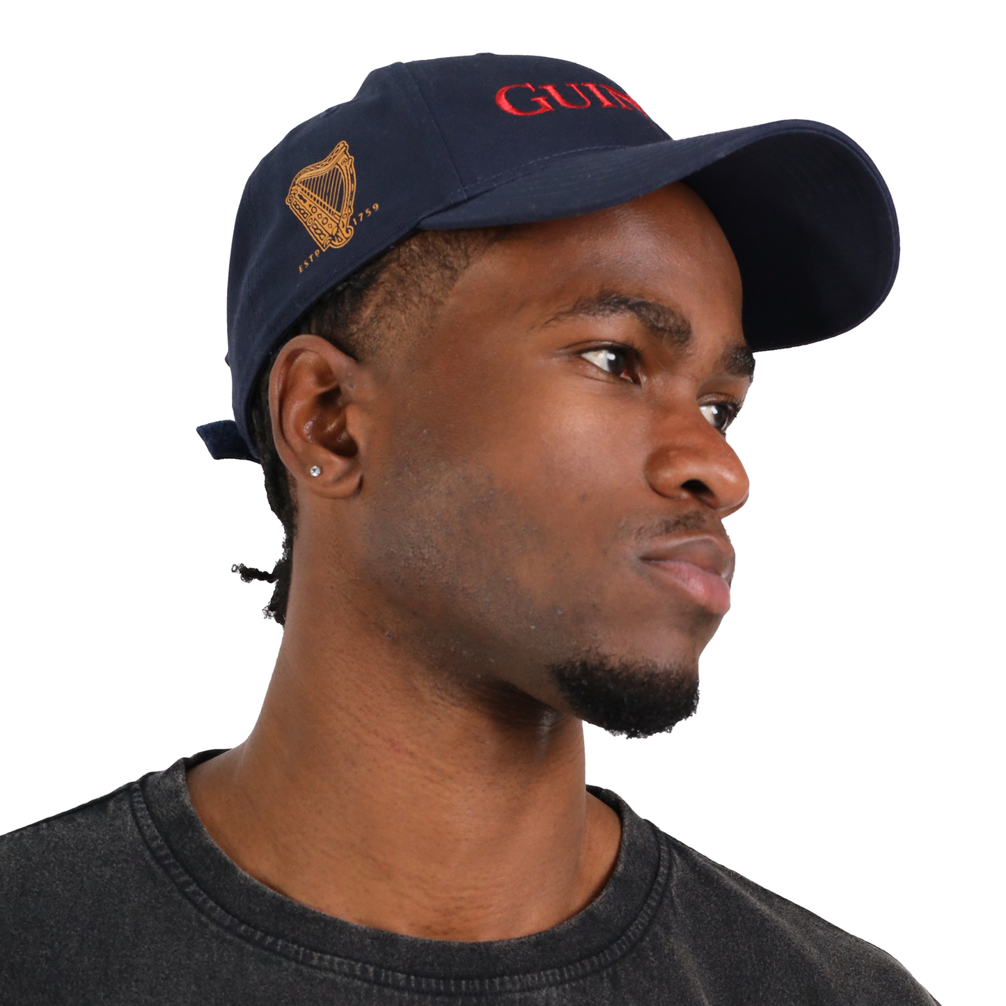 Person wearing a navy blue Guinness Baseball Cap from the Transport Collection by Guinness Webstore US, featuring a gold harp logo on the side, looking to the right.