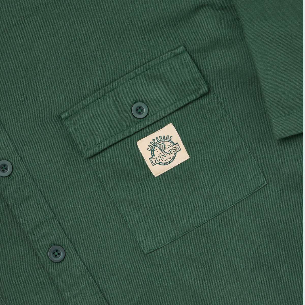 Close-up of a green Guinness Cooperage Work Shirt with a chest pocket, featuring a rectangular “Courage Unlaced” patch sewn onto the pocket.