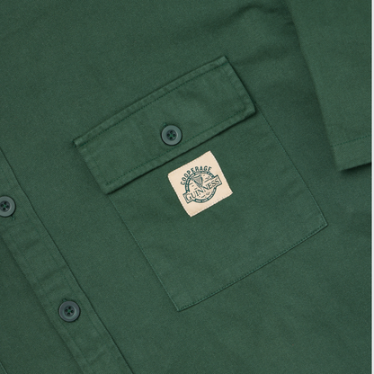 Close-up of a green Guinness Cooperage Work Shirt with a chest pocket, featuring a rectangular “Courage Unlaced” patch sewn onto the pocket.
