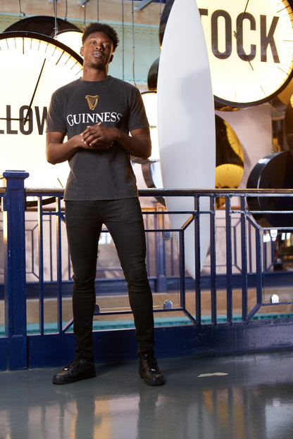 A man wearing a Guinness Distressed Trademark Label T-Shirt, standing in front of a distressed trademark label clock.