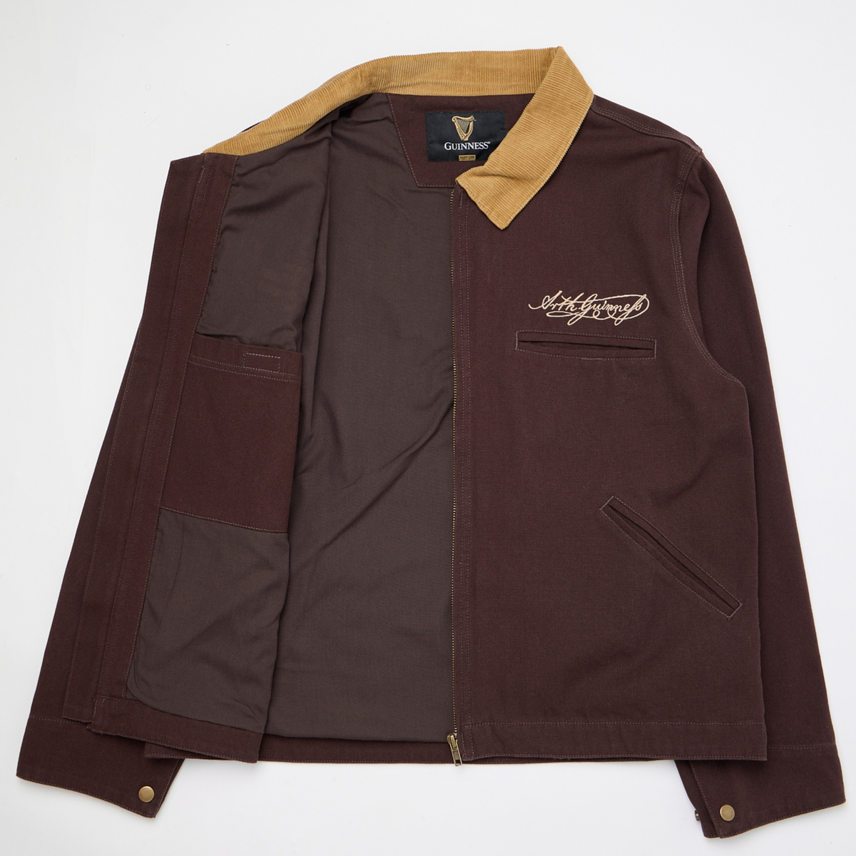 The Guinness Cooperage Work Jacket is a brown heavyweight cotton canvas jacket with a tan corduroy collar, neck branding, and Arthur Guinness’s signature on the chest.