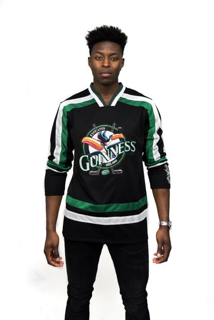 A man faces forward wearing the Guinness Toucan Hockey Jersey in black and green, featuring an embroidered toucan logo, with a plain white background.