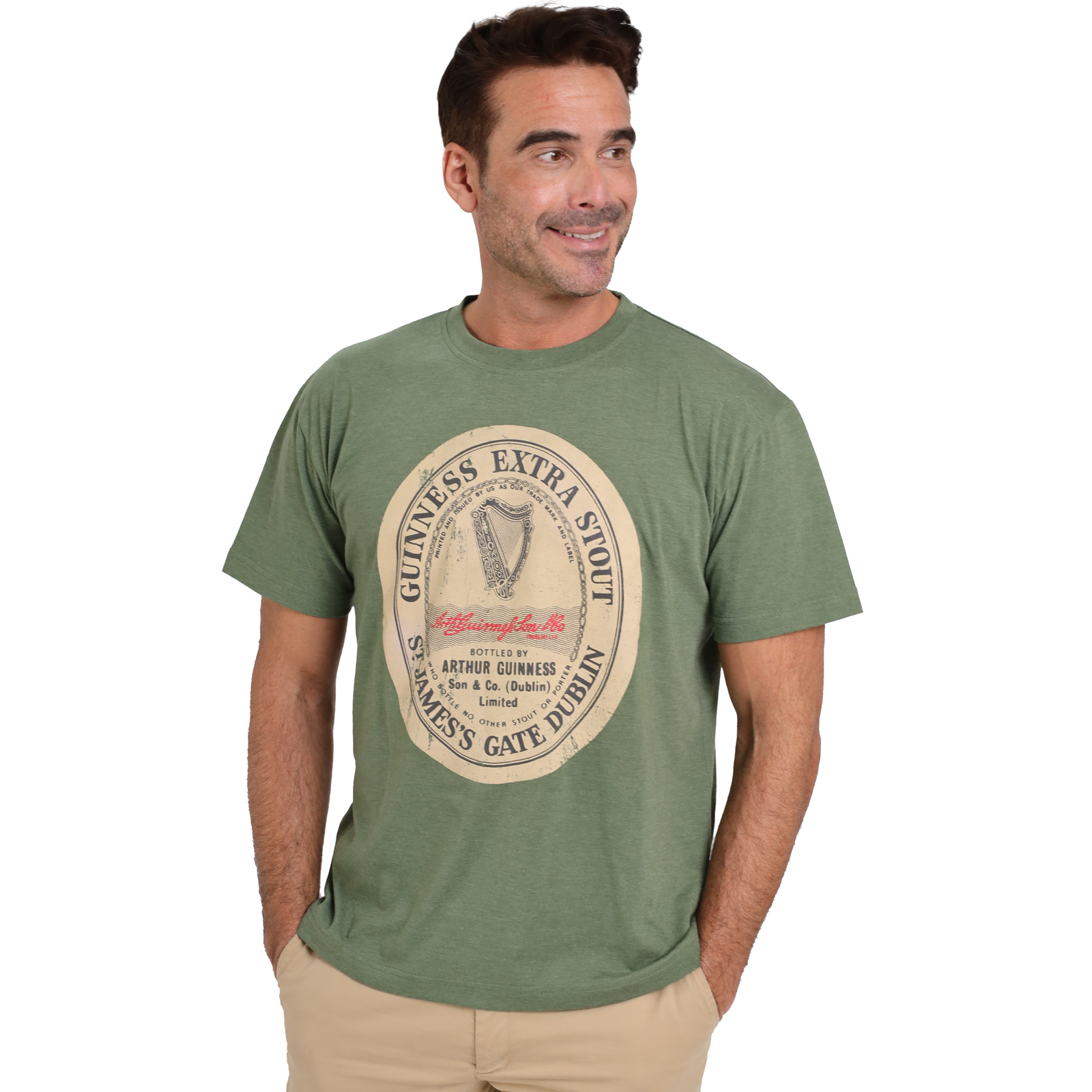 Man wearing a Guinness Green Distressed Label Tee made from a soft cotton blend fabric and beige pants, standing with his hands in his pockets.