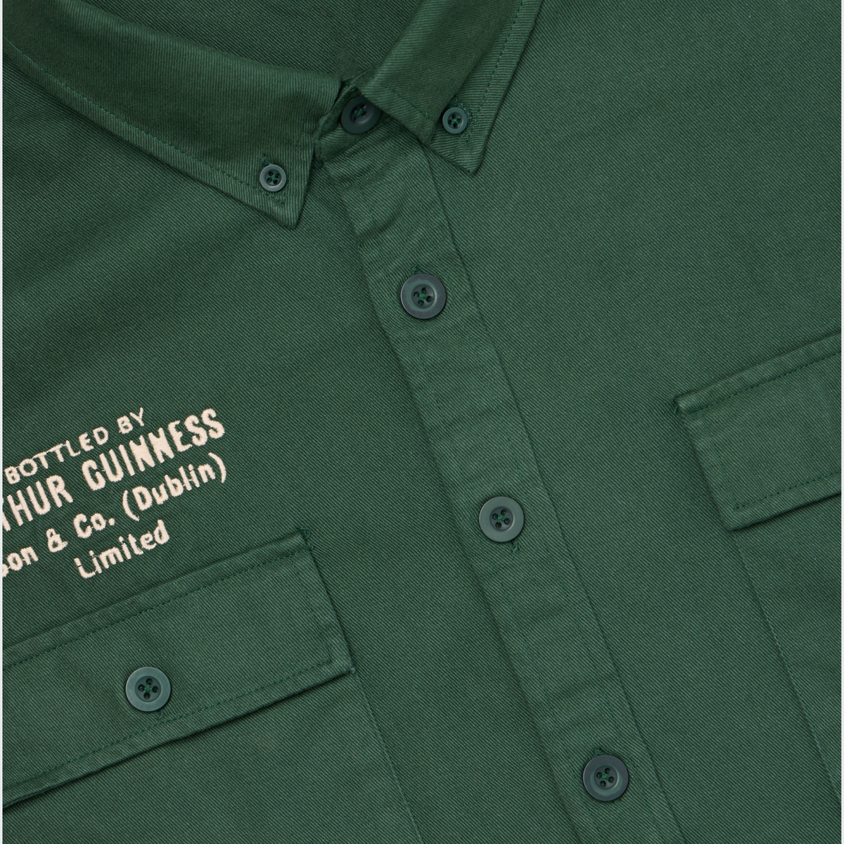 The Guinness Cooperage Work Shirt is dark green with two front pockets and “BOTTLED BY ARTHUR GUINNESS Son & Co. (Dublin) Limited.” embroidered in white.