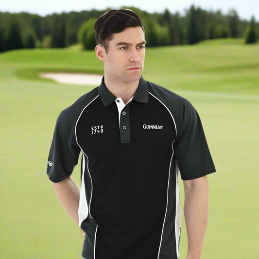 A man wearing a black and white Guinness Performance Golf Shirt, made from moisture-wicking fabric, stands on a grassy golf course with trees in the background.