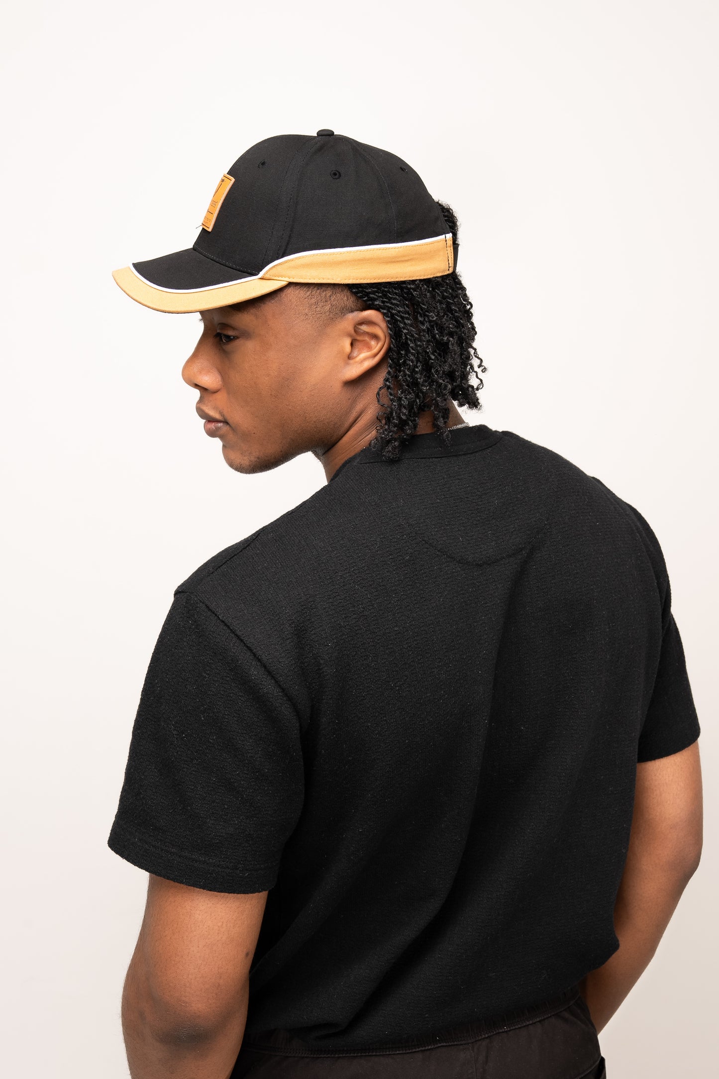 A person wearing a black t-shirt and the Guinness Black Cap with Caramel Edge from Guinness Webstore US, shown from the back and looking over their shoulder.