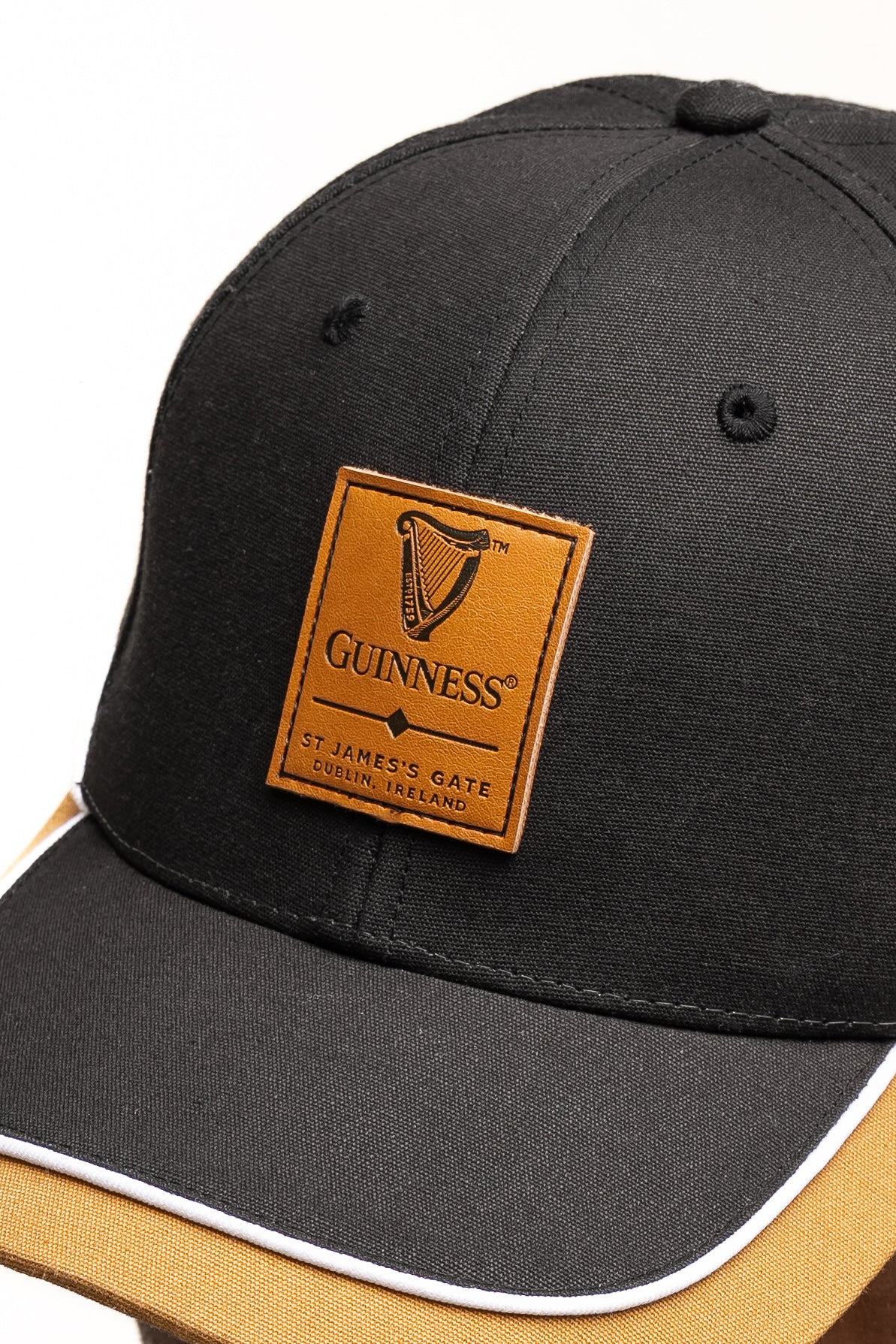 The Guinness Black Cap with Caramel Edge from Guinness Webstore US features a brown leatherette patch showing the iconic harp and "St. James's Gate, Dublin, Ireland"—a perfect addition for any Irish drink fan.
