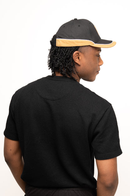 A person wearing a black t-shirt and a Guinness Black Cap with Caramel Edge from Guinness Webstore US is facing away from the camera, displaying the back of their head and upper body.