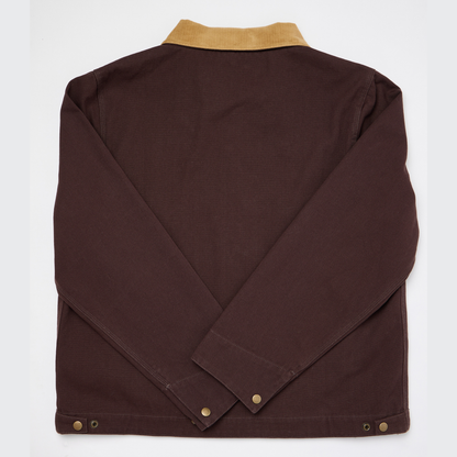 The Guinness Cooperage Work Jacket is a heavyweight cotton canvas jacket with a tan corduroy collar, long sleeves, and button details on the cuffs and hem.