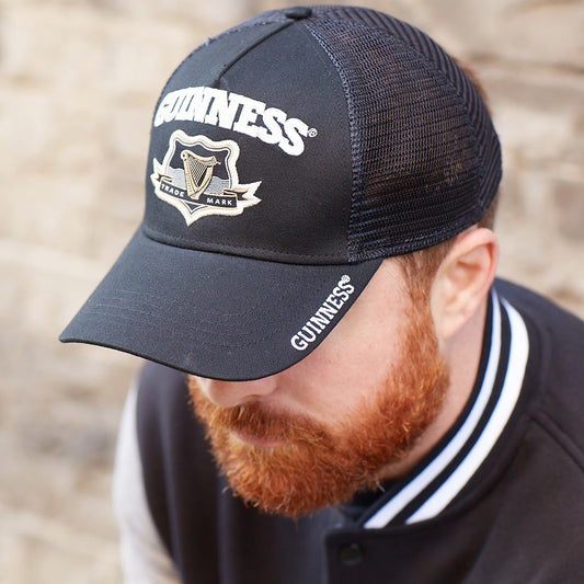 A bearded man sporting a Guinness Signature Black Trucker Mesh Baseball Cap Adjustable.