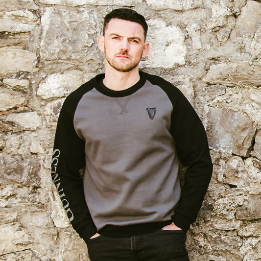 A man leaning against a stone wall wearing a Guinness Long Sleeve Sweater.