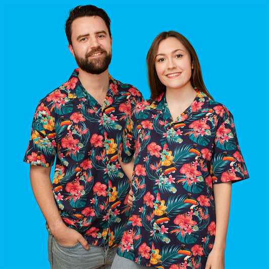 A man and woman wearing a Guinness Toucan Hawaiian shirt surrounded by tropical plants and flowers.