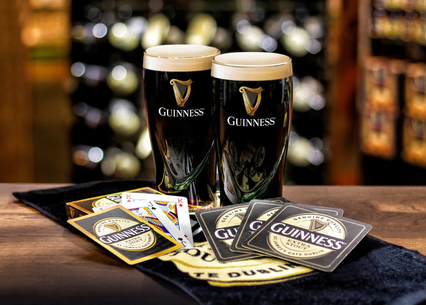 Two Guinness Home Bar Pack pint glasses and playing cards on a table.