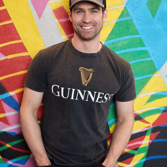 A man wearing a Guinness® Distressed Trademark Label T-Shirt leaning against a colorful wall.