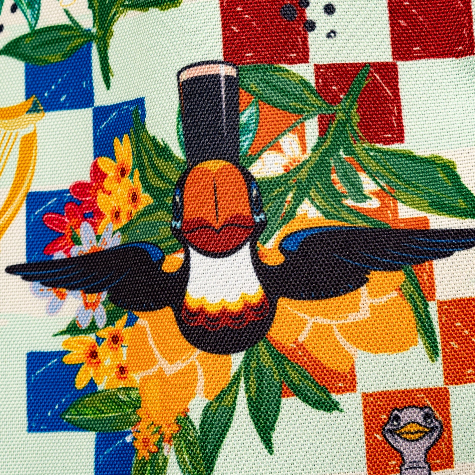 The Guinness Webstore US Guinness Toucan Beach Bag features a bold Hawaiian print with a toucan, yellow flowers, and green leaves on a red and blue checkerboard background. This vibrant 20L bag is perfect for your next beach outing.