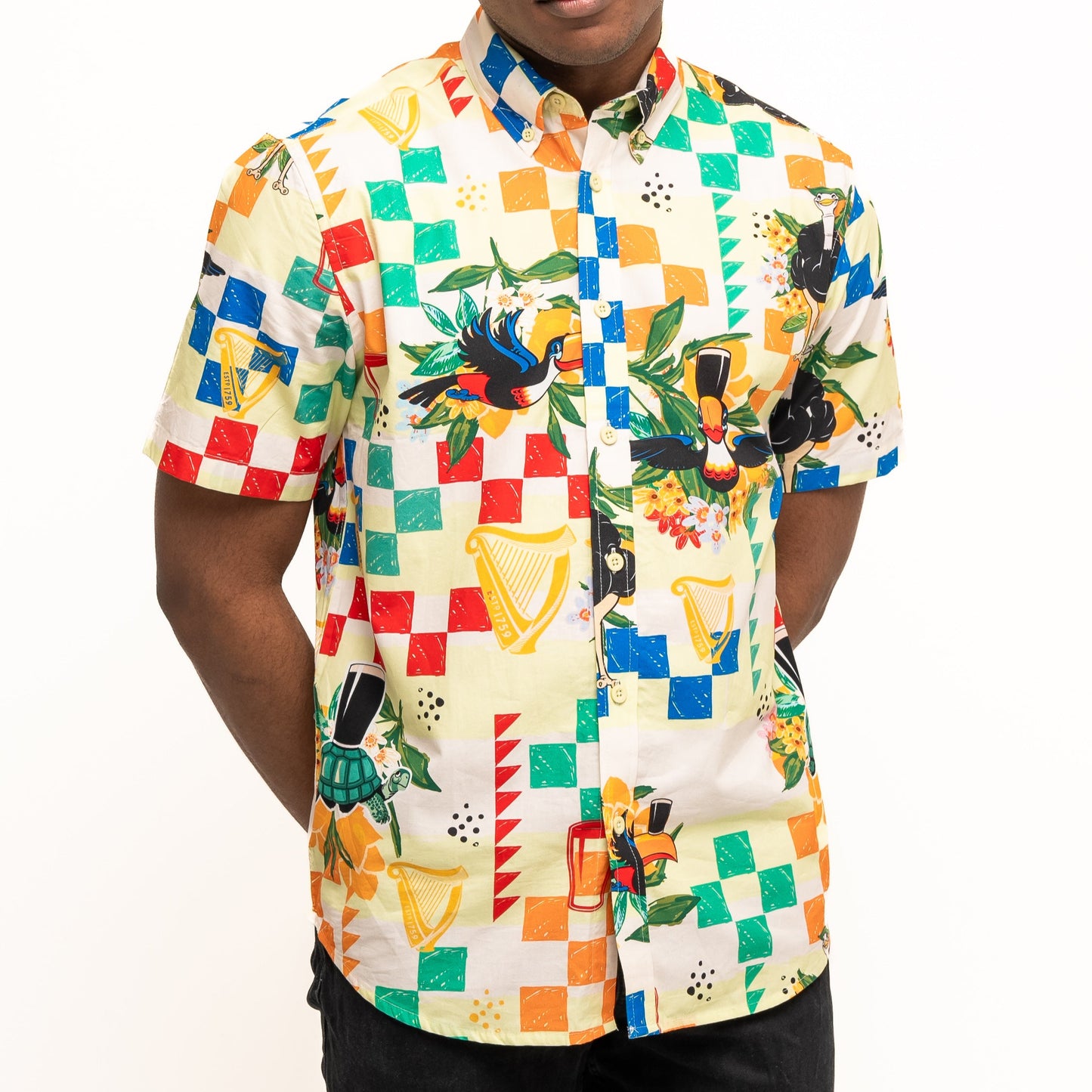 A person wears the Guinness Toucan Beach Shirt by Guinness Webstore US, a short-sleeve Hawaiian button-up with colorful geometric and musical instrument prints, made of breathable woven cotton, standing against a plain white background.