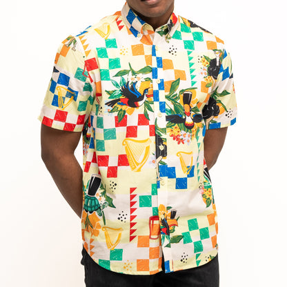 A person wears the Guinness Toucan Beach Shirt by Guinness Webstore US, a short-sleeve Hawaiian button-up with colorful geometric and musical instrument prints, made of breathable woven cotton, standing against a plain white background.
