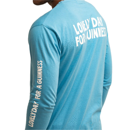 Wearing the Guinness Seb Curi Lovely Day Longsleeve Tee - Blue from Guinness Webstore US, this light blue shirt showcases “LOVELY DAY FOR A GUINNESS” in white on the back and sleeve—a stylish Sebastian Curi collaboration.
