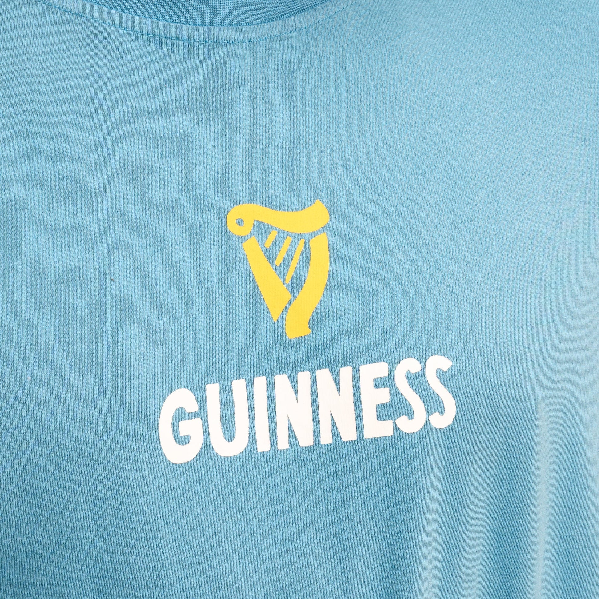 The Guinness Seb Curi Lovely Day Longsleeve Tee in blue from Guinness Webstore US features a yellow harp above "GUINNESS" in white, styled with pop-art flair.