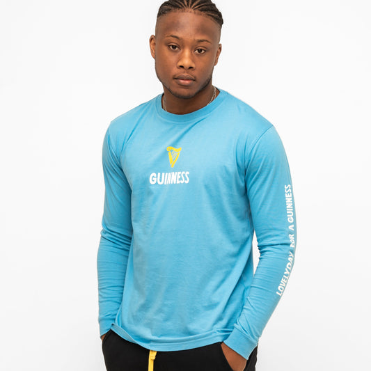 A man wears the blue Guinness Seb Curi Lovely Day Longsleeve Tee from Guinness Webstore US with white text, standing against a plain white background.