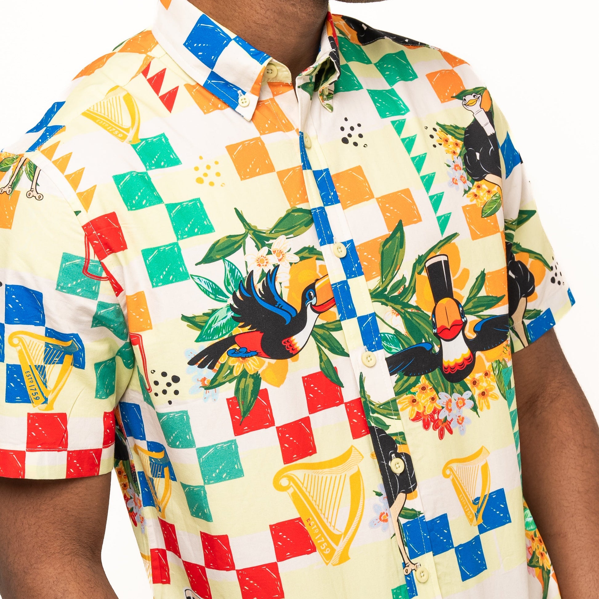 A person wearing the Guinness Toucan Beach Shirt from Guinness Webstore US—a Hawaiian-style, short-sleeve button-up with toucans, harps, and floral designs in colorful, breathable woven cotton.