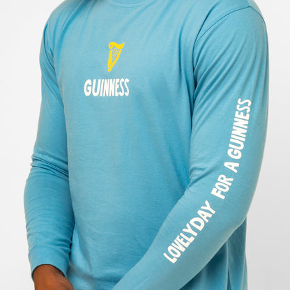 Wearing the Guinness Seb Curi Lovely Day Longsleeve Tee - Blue by Guinness Webstore US, a pop-art style blue tee featuring “GUINNESS” and a harp on the chest, with “LOVELY DAY FOR A GUINNESS” printed on the sleeve.