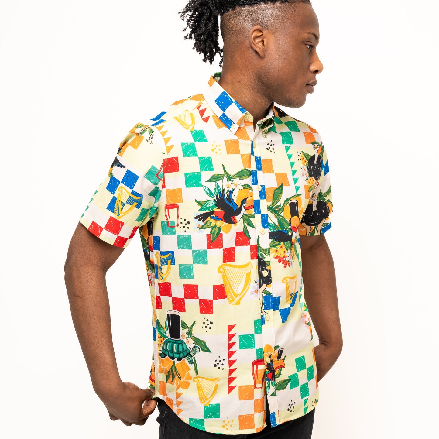 A person stands sideways wearing the Guinness Toucan Beach Shirt by Guinness Webstore US—a short-sleeve, button-up with a colorful geometric and graphic print on breathable woven cotton over a white background.
