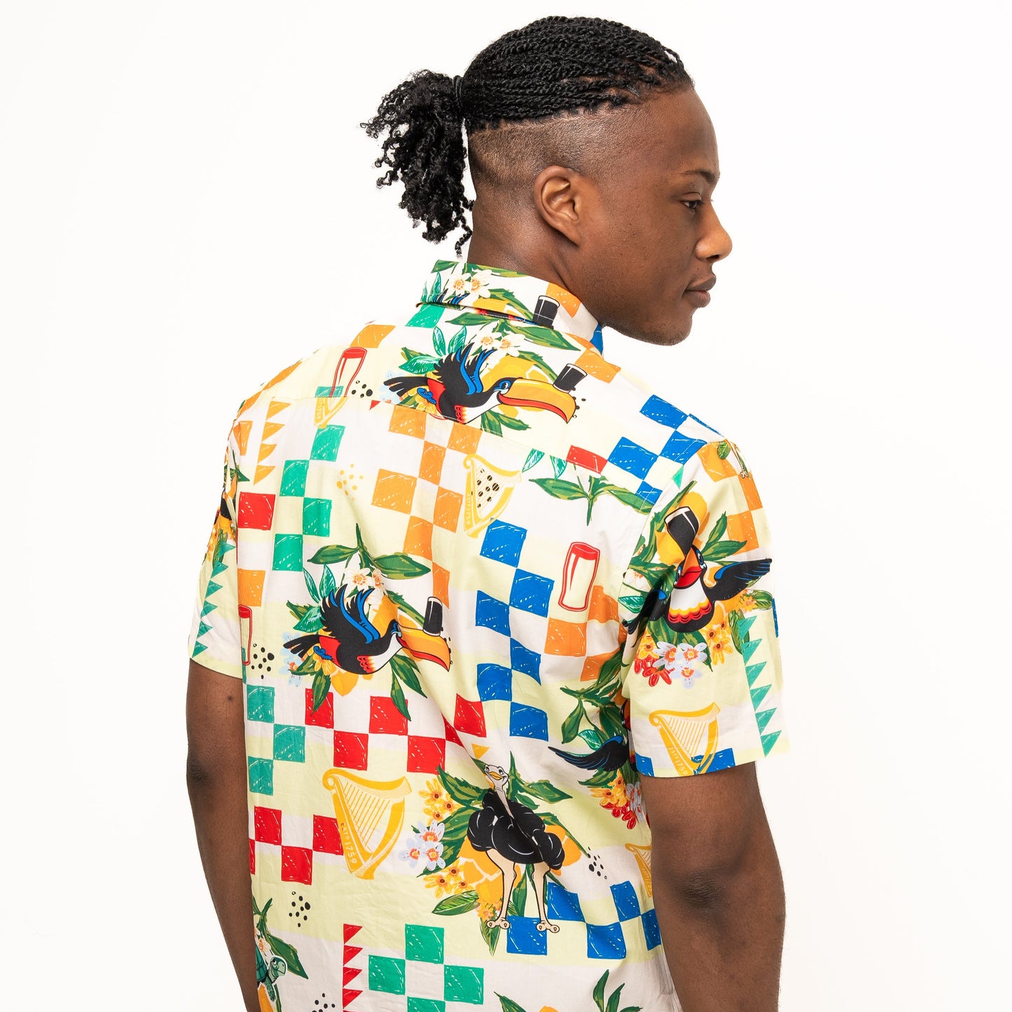A man with braided hair in a ponytail is seen from the back wearing a vibrant Guinness Toucan Beach Shirt by Guinness Webstore US, made of breathable woven cotton in bold Hawaiian style, set against a plain white background.