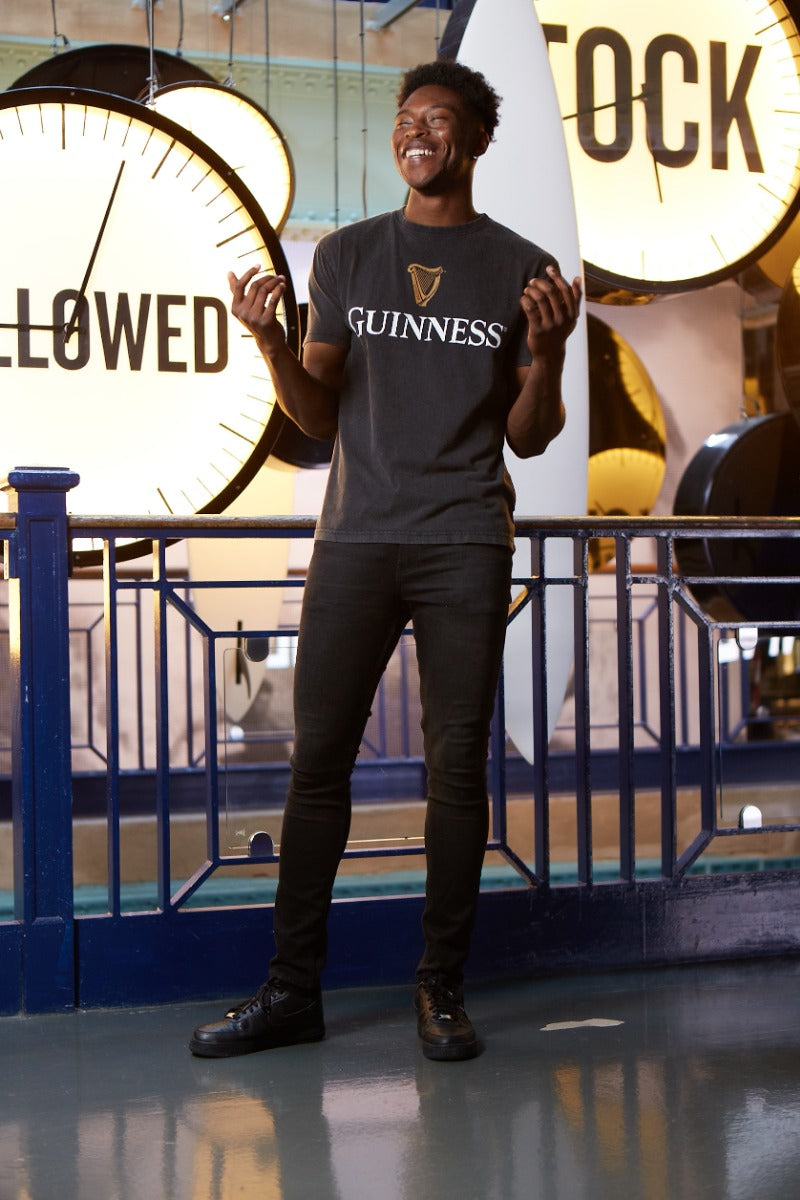 A man wearing a Guinness® Distressed Trademark Label T-Shirt stands in front of a clock.