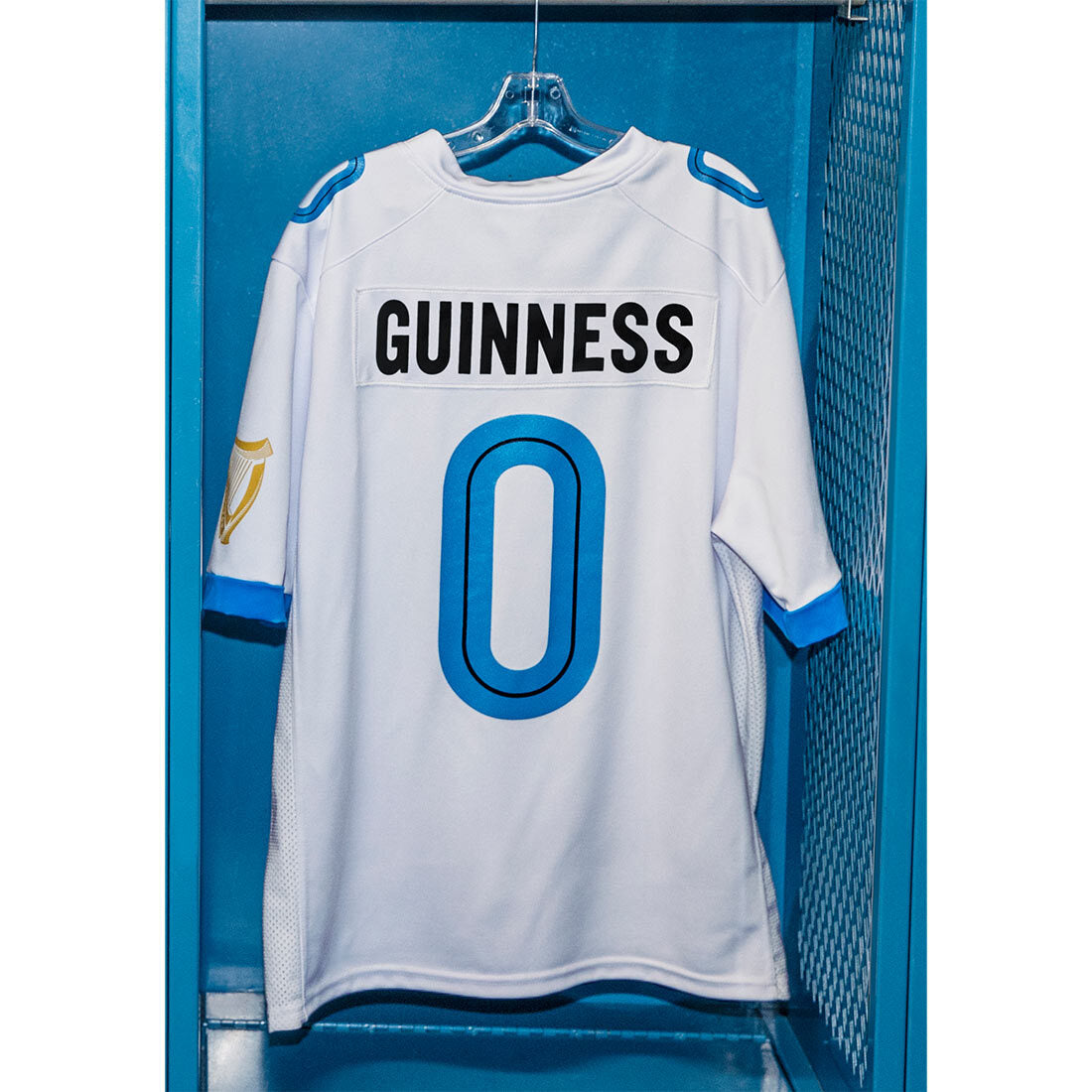A Guinness Webstore US white football jersey with the blue number 0 hanging in a locker.