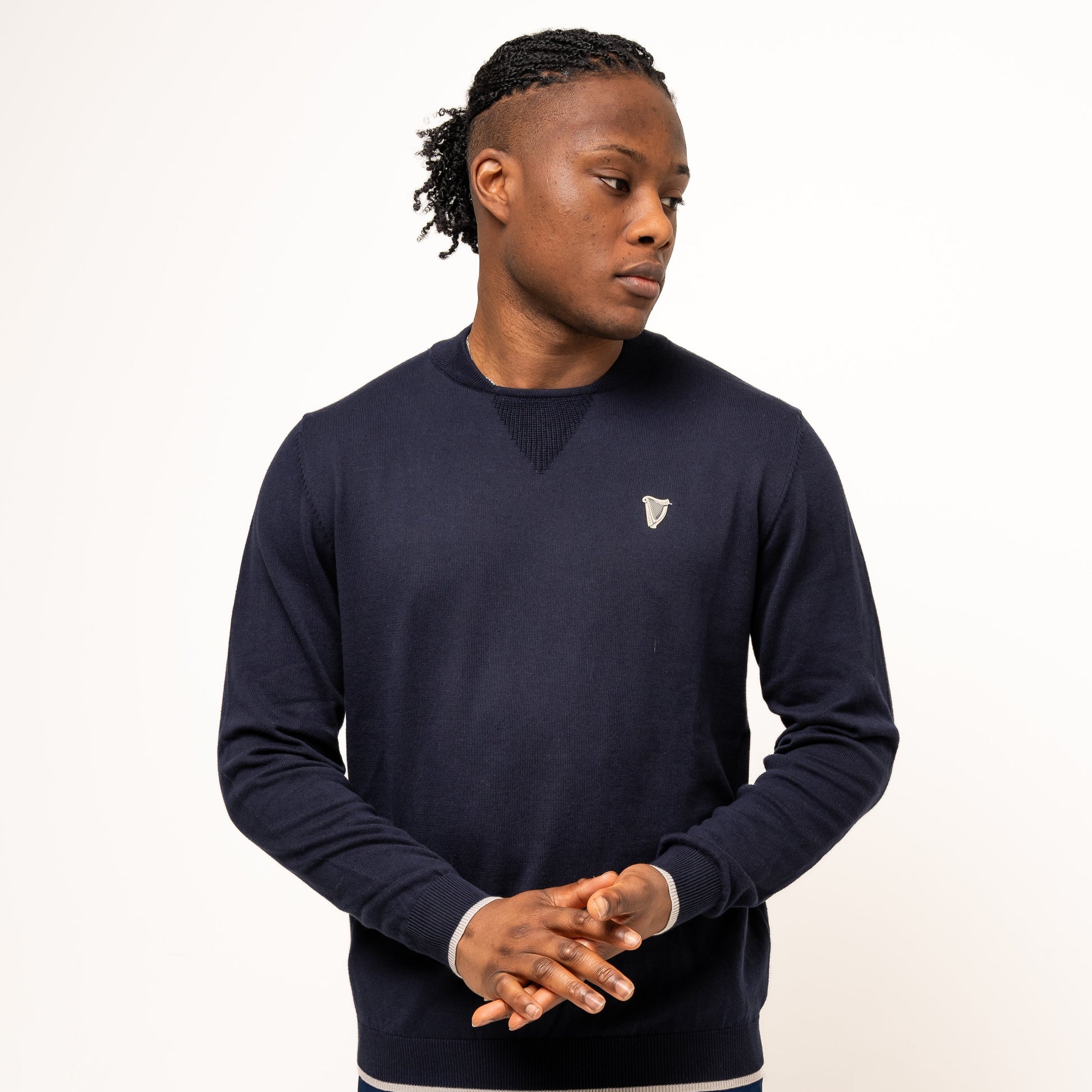 Wearing the Guinness Webstore US Performance Cotton Sweater in navy, a man stands against a white background in navy shorts, hands clasped, looking left—ready for golf in comfortable, moisture-wicking cotton.