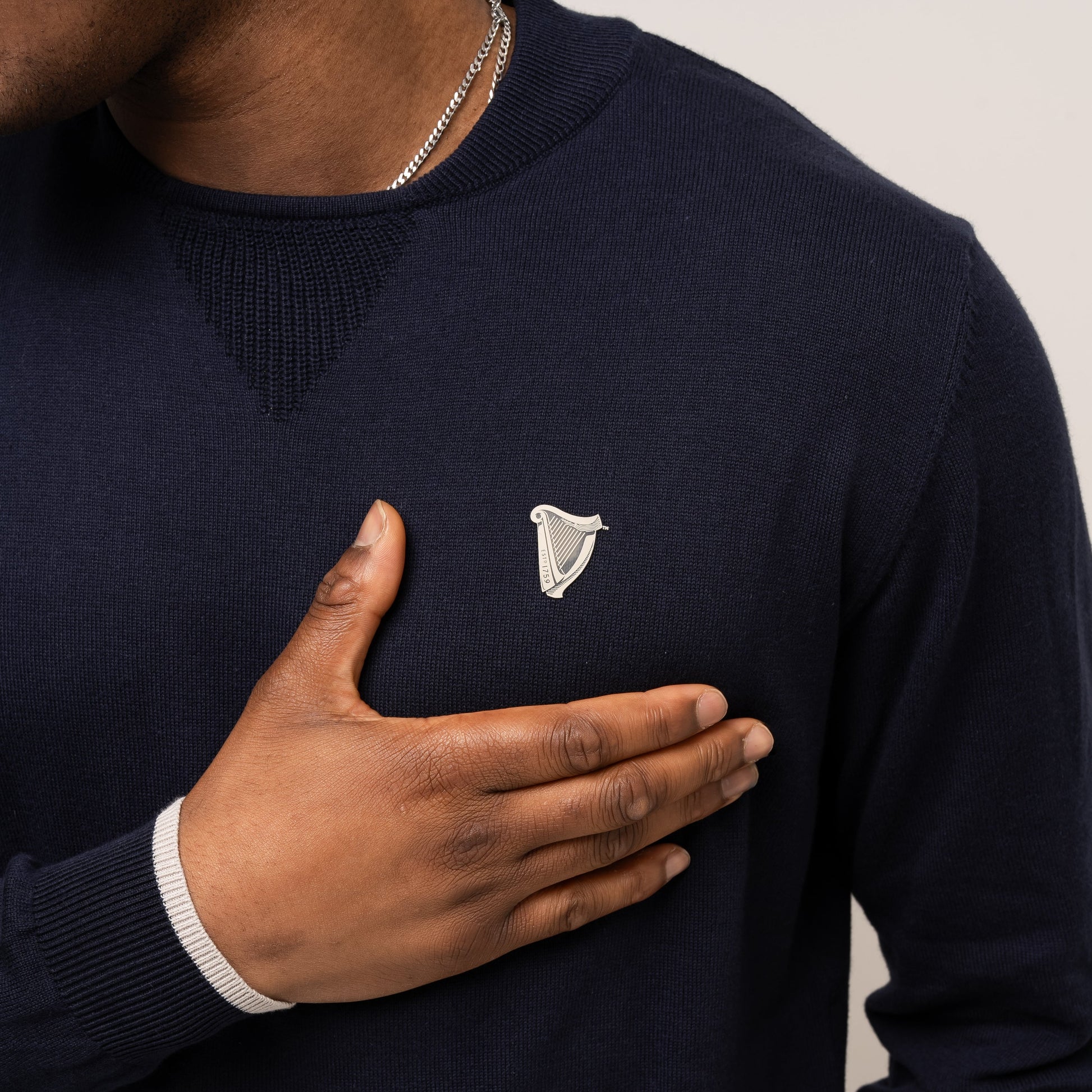 Wearing the Guinness Performance Cotton Sweater - Navy from Guinness Webstore US, a person places their right hand over their chest; made from moisture-wicking cotton, it’s a perfect choice for the golf course.