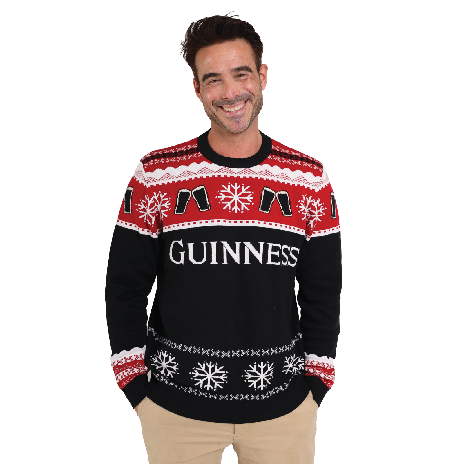 A man smiles with hands in pockets, wearing the Official Guinness Holiday Sweater—a festive red, black, and white knit featuring snowflake patterns and "Guinness" on the front—perfect for any holiday wardrobe.