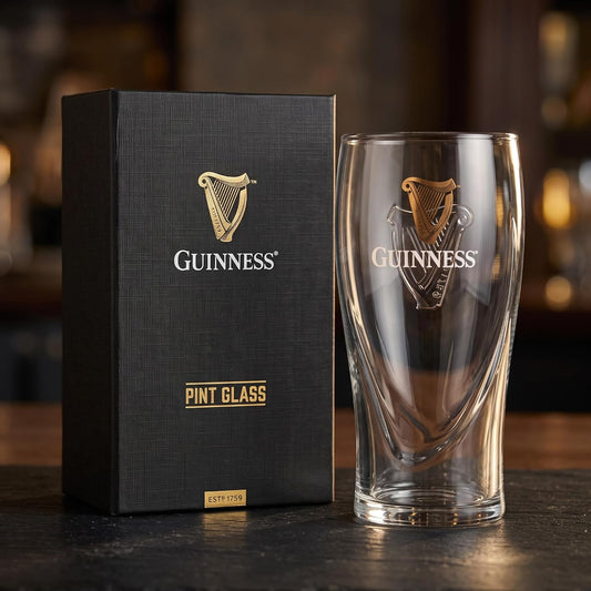 A Guinness® Pint Glass with Gift Box featuring a harp logo standing next to its black presentation box.