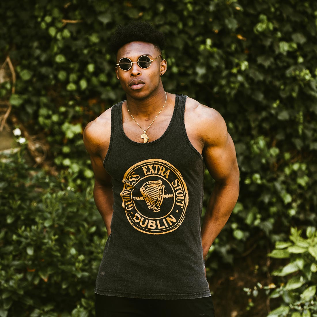 A young man wearing a Guinness Washed Extra Stout Tank Top and sunglasses enjoys the summer months sipping on a refreshing Guinness.
