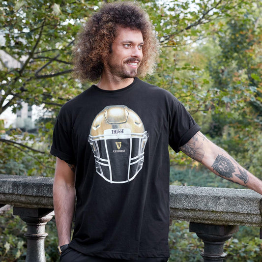 A man wearing a Guinness Notre Dame Helmet T-Shirt Black.