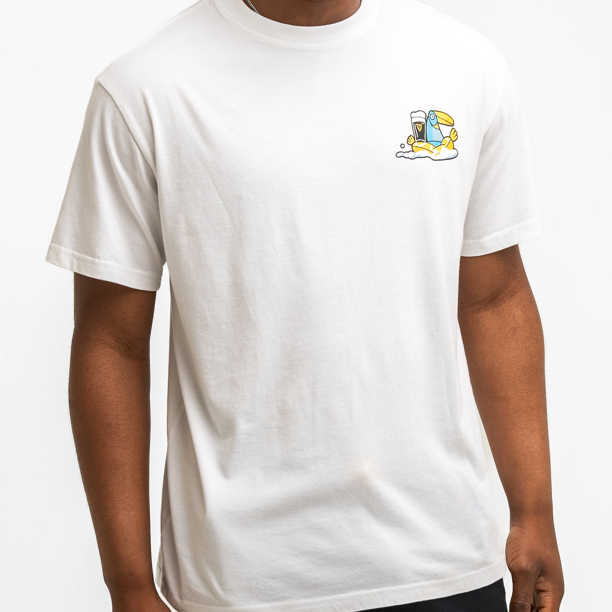 A person wearing the Guinness Seb Curi Oversize Tee in white from Guinness Webstore US, featuring a small, colorful beach-themed graphic on the upper left chest.